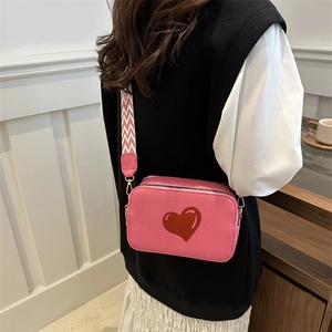 Pink heart camera bag with wide geometric strap and pebbled leather texture