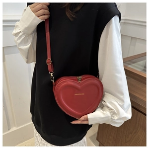 Close-up of a red heart-shaped shoulder bag with gold hardware and fashion text