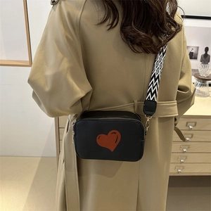 Minimalist black camera bag for women featuring a red heart print and wide woven strap