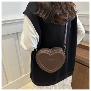 Brown heart-shaped crossbody bag with gold hardware shown from behind on a model