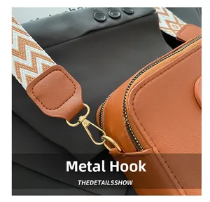 Close-up of golden metal hooks and textured strap on a brown leather camera bag