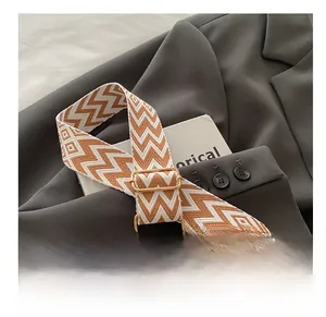 Detail of adjustable woven wide shoulder strap with geometric pattern and gold hardware