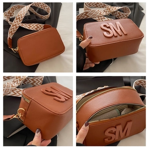 Detail view of brown cross-grain camera bag with SM logo and geometric wide strap