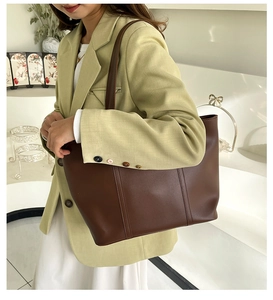 Detail of a large brown leather tote bag with smooth texture and vertical stitching