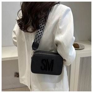 Detail of black pebbled leather camera bag with 3D letters and patterned wide strap