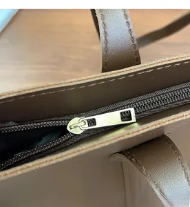 Detail of smooth light gold metal zipper and neat stitching on brown leather tote bag