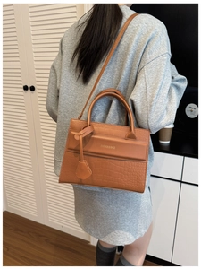 Close-up of brown textured crossbody bag with crocodile pattern and metal logo lettering