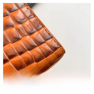 Detailed macro view of the glossy orange-brown crocodile embossed leather with sharp stitching