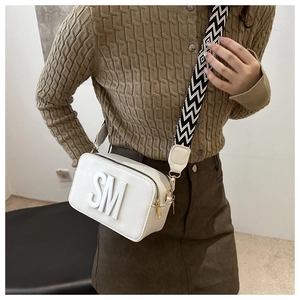 Detail of white minimalist camera bag with wide woven strap and SM letter decor