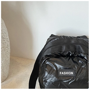 Detailed view of black quilted puffer shell bag with Fashion label and glossy texture