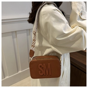 Detail of a brown camera bag with wide ethnic strap and SM logo shown on a model