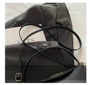 Détail du sac à main noir en cuir grainé avec bandoulière fine réglable sur un veston
