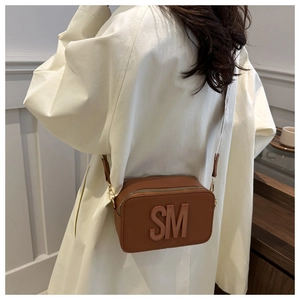Close-up of brown camera bag with embossed letters and adjustable wide shoulder strap