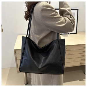 Close-up of minimalist black tote bag featuring soft pleated PU leather and long shoulder strap
