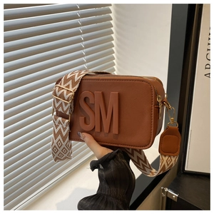 Detail of brown cross-grain leather camera bag with wide geometric woven shoulder strap