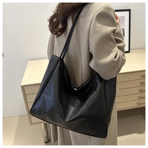 Detailed view of the large black tote bag carried over the shoulder of a beige wool coat