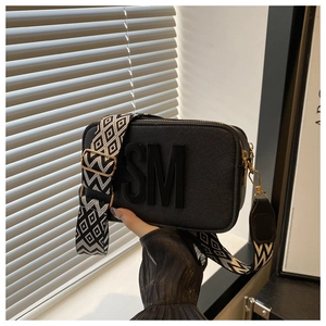 Detail of black crossbody camera bag featuring 3D letters and a wide geometric strap