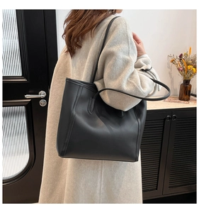 Elegant large black leather tote bag worn over the shoulder by a model in office setting