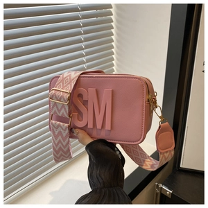 Detail of pink camera bag with SM embossed logo and geometric pattern wide strap