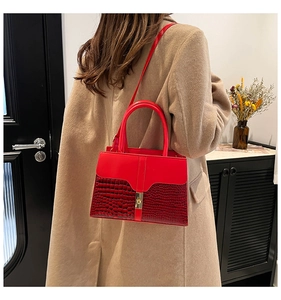 Detailed view of a red leather crossbody bag with crocodile texture on a beige coat