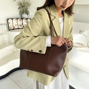 Detail view of large dark brown leather tote bag held by model in light green blazer