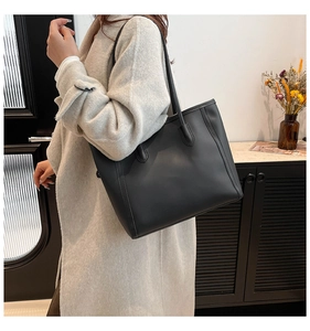 Minimalist matte black leather tote bag shown on model in a stylish home setting