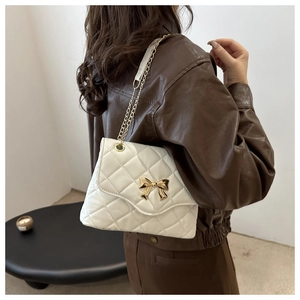 Close-up of creamy white quilted crossbody bag with golden bow clasp on model arm