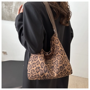 Detail of leopard print tote bag with brown leather strap worn over a black coat