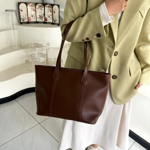 Detail of a large dark brown tote bag styled with a professional suit for daily commuting