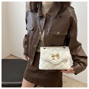 Close-up of a white quilted crossbody bag with a gold bow buckle on a model wearing a jacket