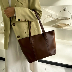Detail of dark brown matte leather tote bag worn by model in minimalist indoor setting