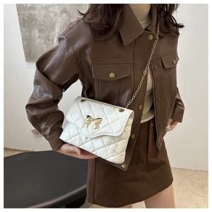 White quilted crossbody bag with gold bow detail worn with brown leather outfit