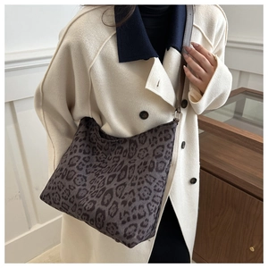 Detail view of leopard print tote bag with brown leather strap on model in beige coat