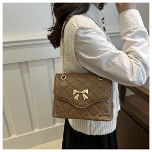 Detail of a brown quilted crossbody bag with a gold bow buckle and elegant chain strap