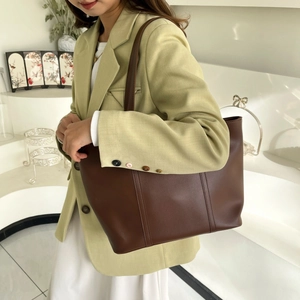 Detail of dark brown leather tote bag with vertical stitching worn by model