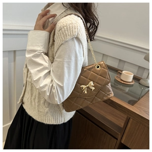 Brown quilted leather chain bag with golden bow clasp shown on a model
