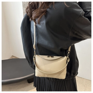 Sac bandoulière beige en cuir avec fermoir doré porté par un mannequin en veste de cuir