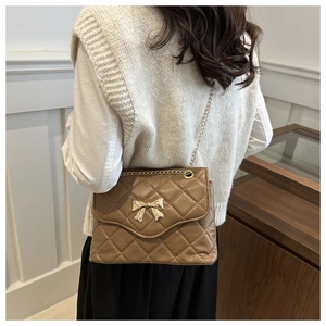 Detail of a brown quilted chain bag with a gold metal bow on the elegant handbag cover