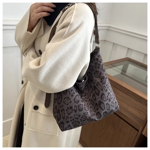 Detail of leopard print hobo bag with brown leather strap worn over a white coat