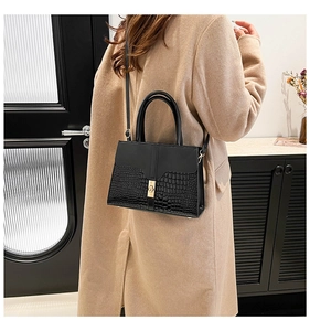 Detail of black crossbody bag featuring crocodile pattern leather and gold square lock