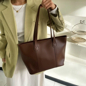 Detail of dark brown matte leather tote bag held by model for casual commuting look