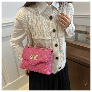 Detail of pink quilted crossbody bag with golden bow clasp and metal chain strap