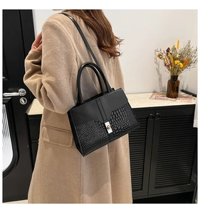 Detail of elegant black tote bag featuring crocodile pattern leather and metal twist lock