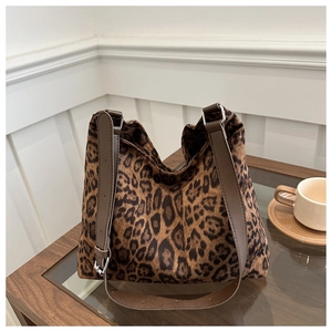 Close-up of leopard print tote bag with brown leather strap and metal buckle on wooden table