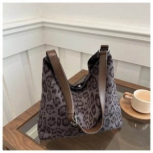Detail of leopard print tote bag featuring brown leather straps on a wooden table