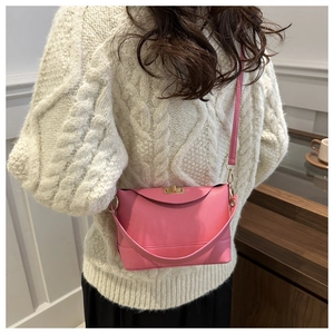 Détail d'un sac rose en cuir grainé avec un fermoir doré porté par un mannequin