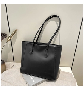 Detail of a large black tote bag featuring matte leather texture and fine stitching