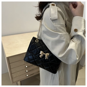 Detail of black quilted shoulder bag featuring gold bow hardware and chain strap