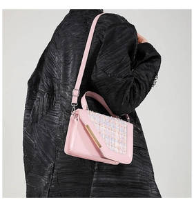 Gros plan du sac bandoulière en tweed rose sur manteau noir avec détails dorés