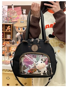 Detail view of black canvas ita-bag featuring a transparent PVC front pocket with plush toy